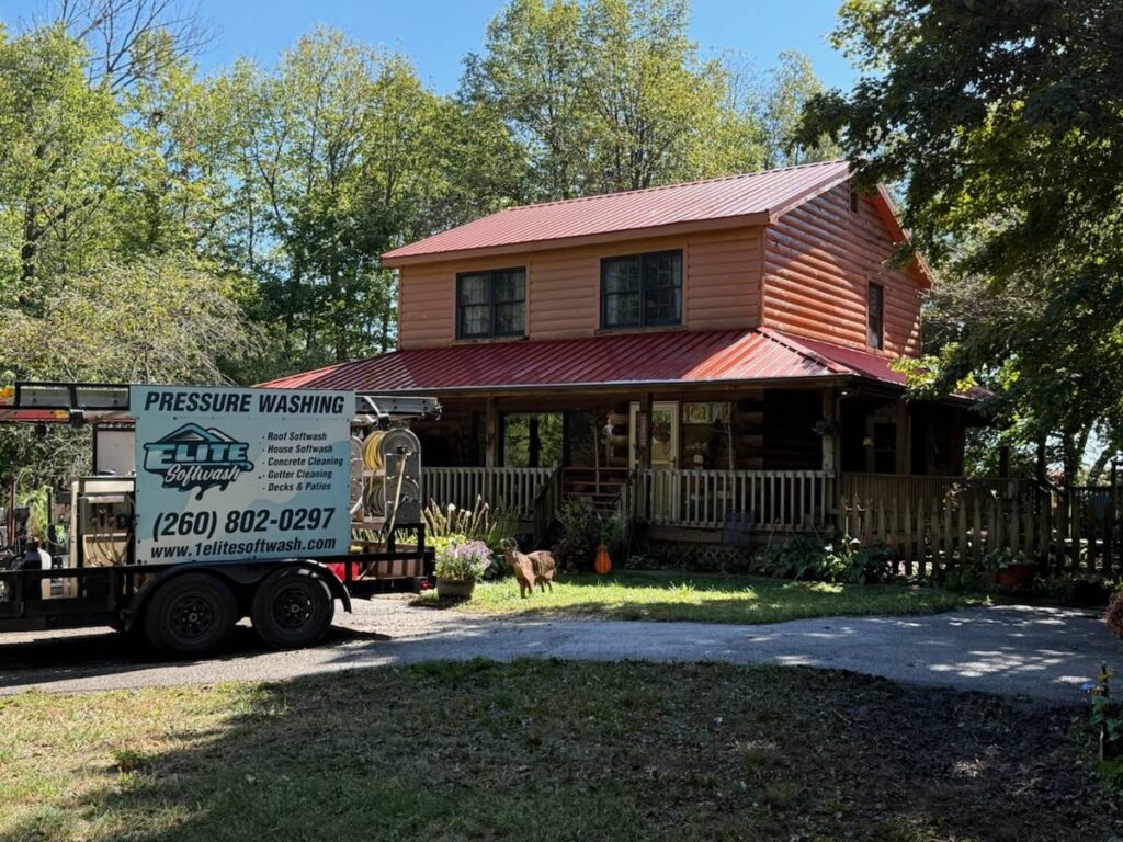 Elite Softwash pressure washing trailer on site at a log home with a red metal roof near Fort Wayne