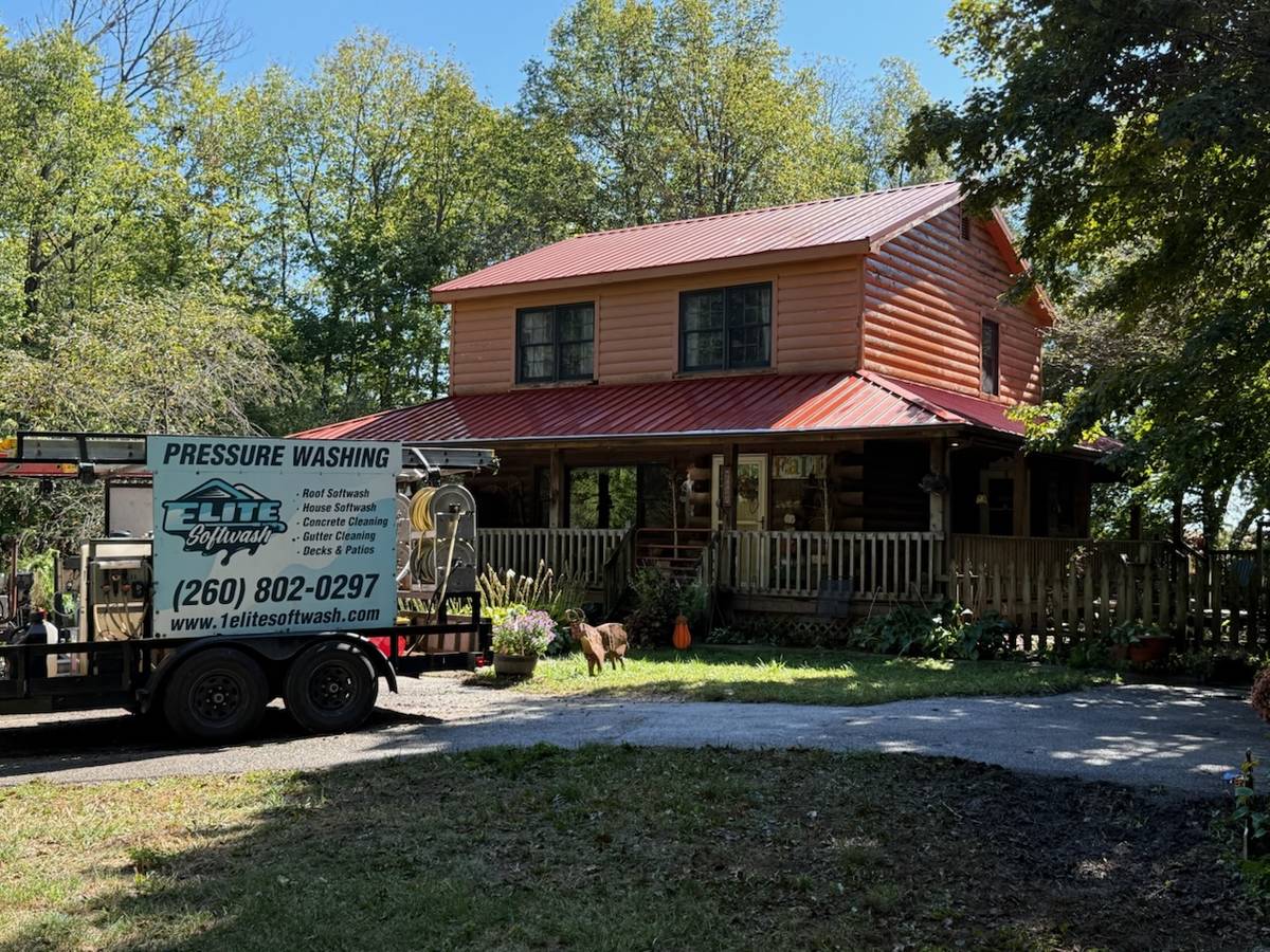 Elite Softwash pressure washing trailer on site at a log home with a red metal roof near Fort Wayne