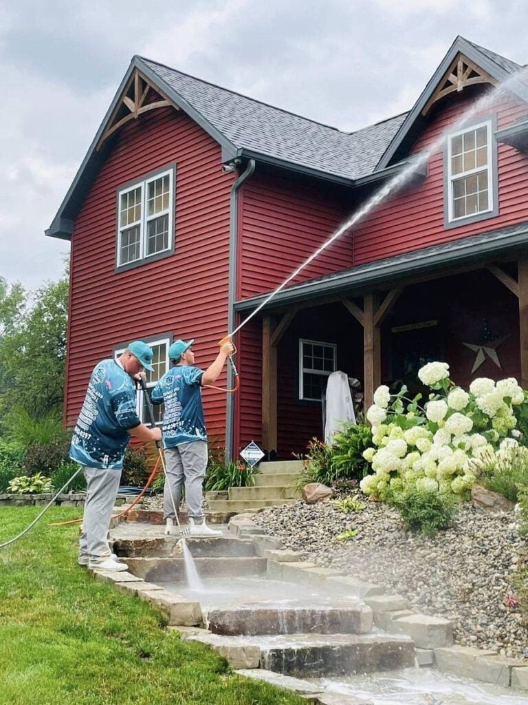 Two Elite Softwash crew members soft washing red siding on a northern Indiana home