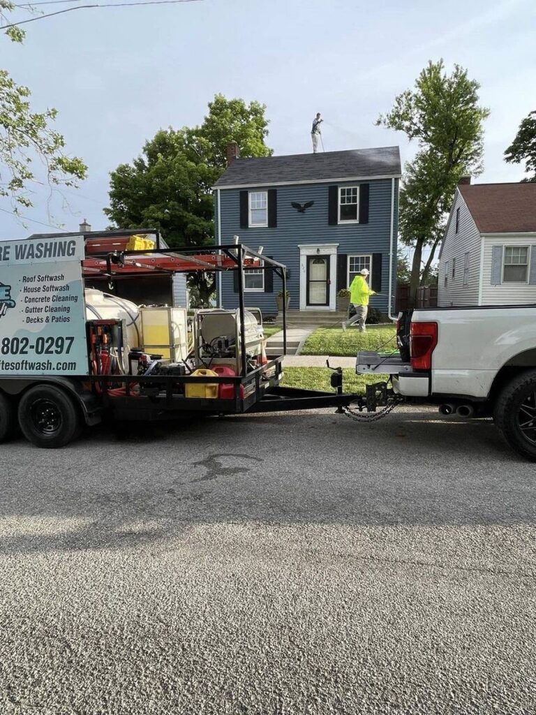 Elite Softwash crew soft washing a shingle roof in Fort Wayne, Indiana with branded trailer in front