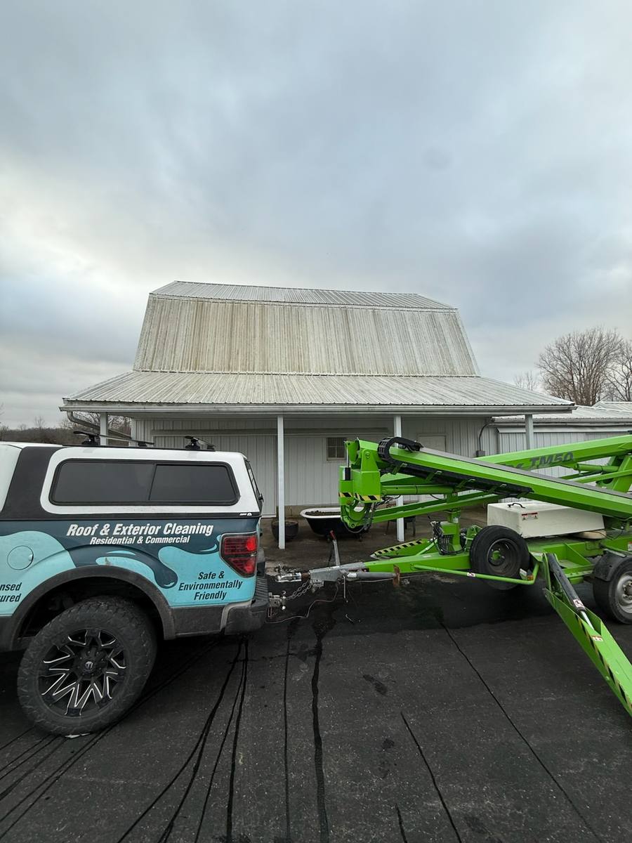 Oxidized metal barn roof before cleaning with Elite Softwash truck and boom lift on site